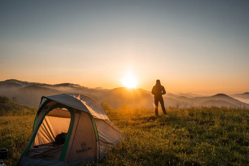 A tent set up on a grassy hill while the sun sets in the background.