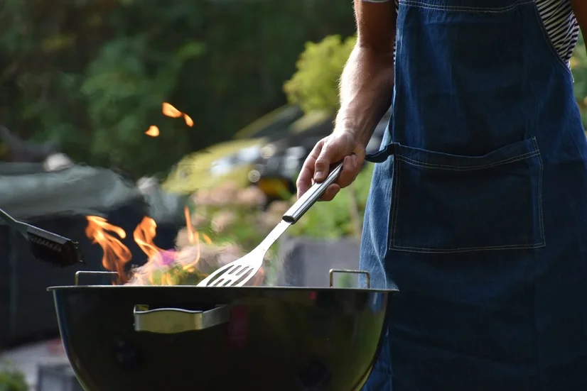 A man in a blue apron using a barbecue.