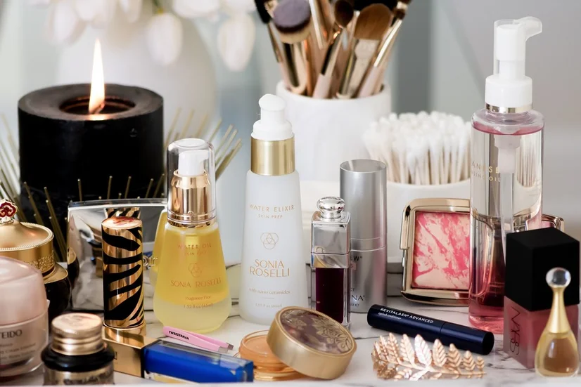 A table covered in makeup and cosmetic products, from face serums to powders and makeup brushes.