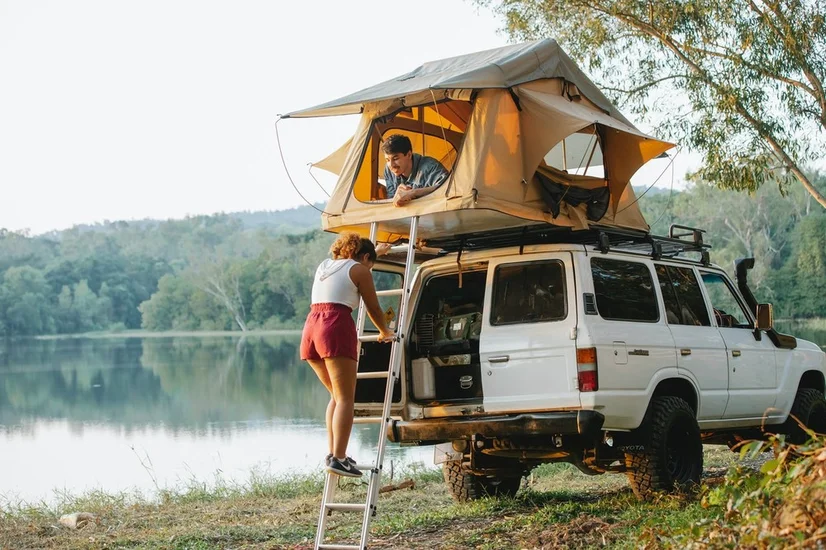 A woman climbing a ladder into a roof top car tent.