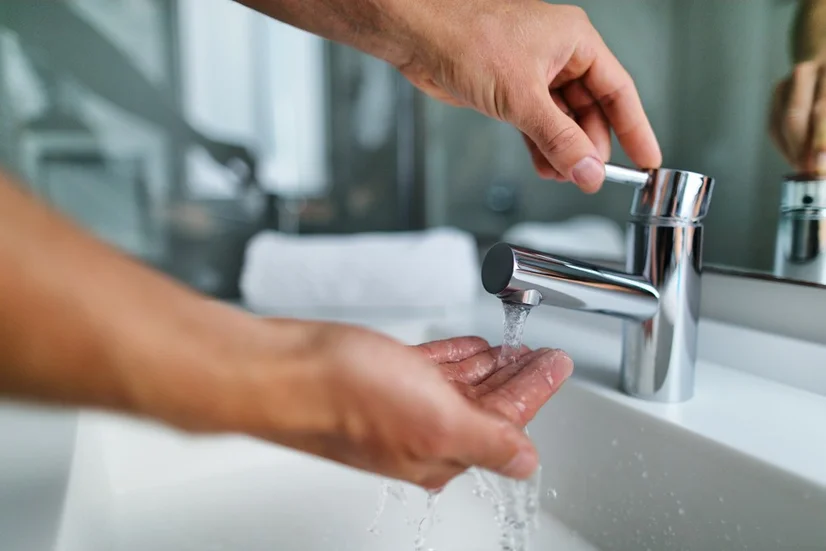 A close up of a man washing their hands under a bathroom faucet.
