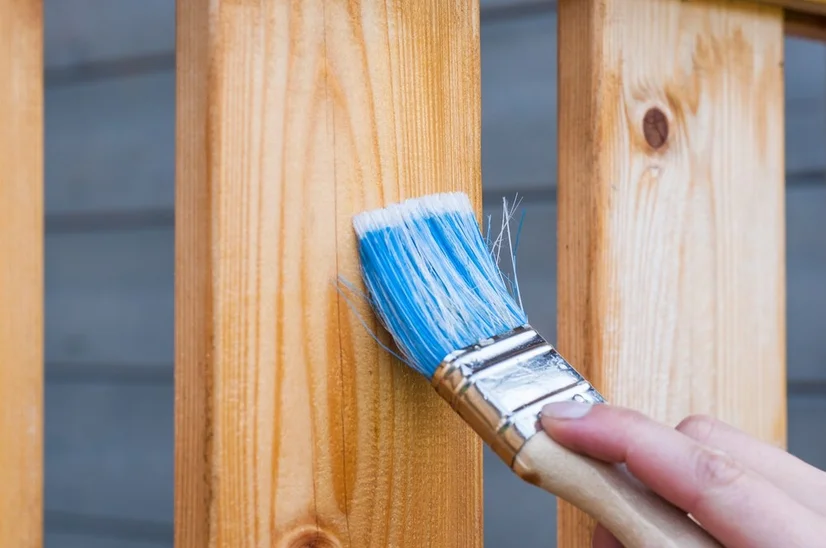 A person using a paintbrush to apply a varnish to a light coloured timber.