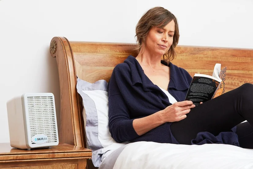 woman reading book with salin salt plus air purifier on night table