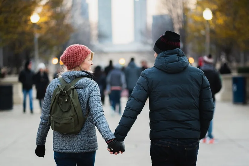 A man and a woman holding hands and walking down a path in the city.