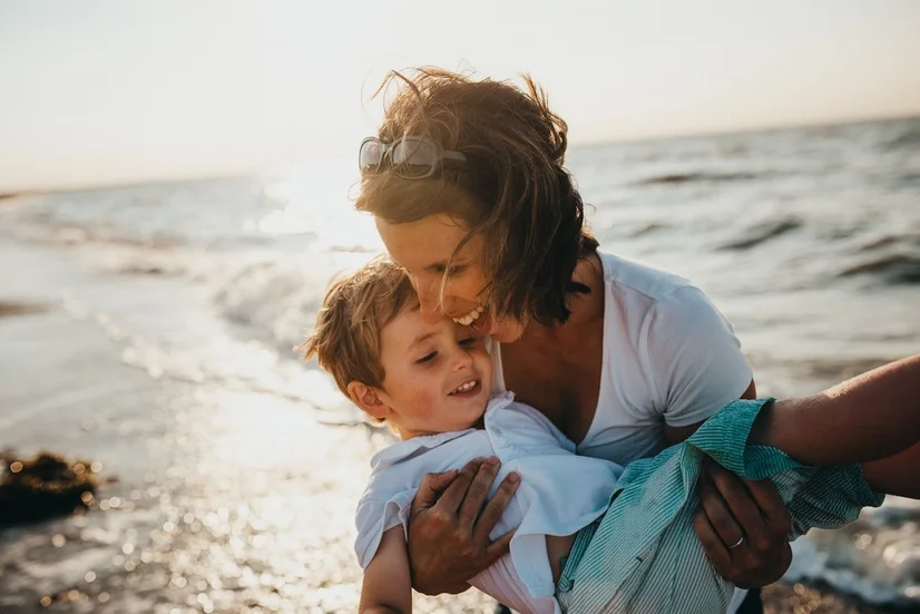 A mother holding her son at the beach.
