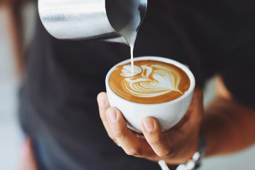 Someone pouring frothed milk into a cup of coffee and making latte art.
