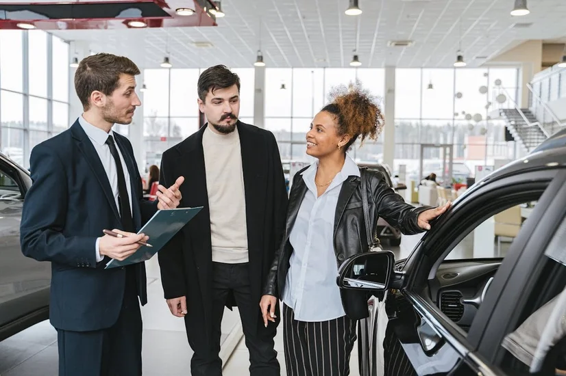 A car salesman showing a couple a car at a car dealership.