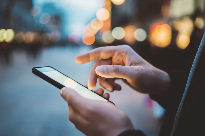 A close up of a man's hands using a smartphone on a street in the evening