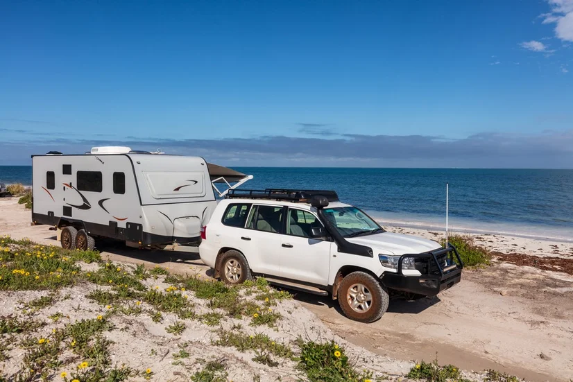 A 4WD towing a white caravan on a sandy track by a beach.