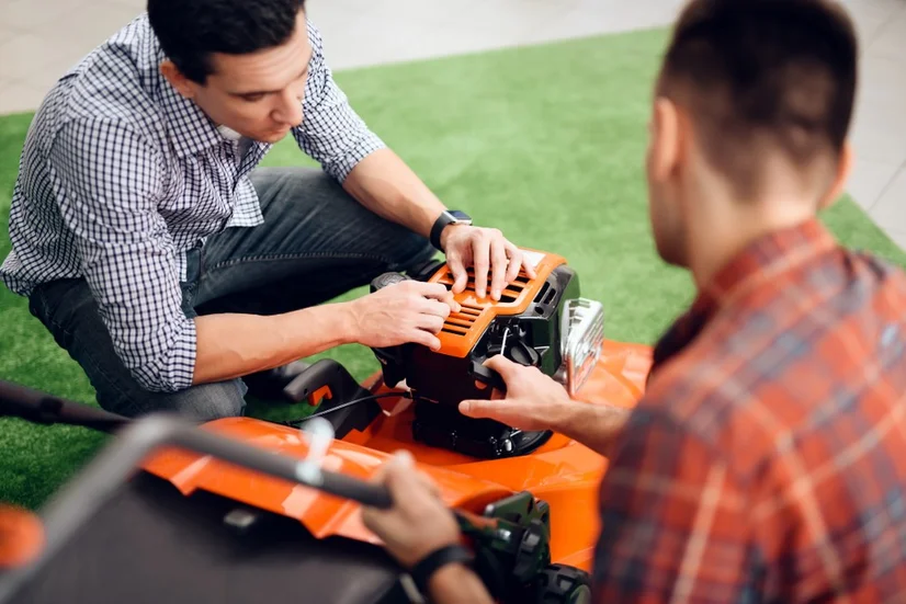 A power tool salesman showing a customer the features of a lawn mower.