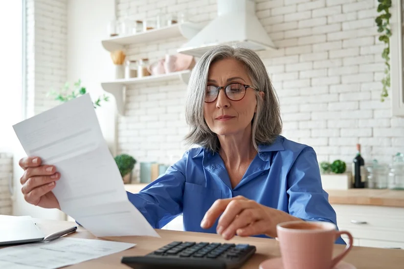 A woman wearing glasses sitting at her dining table and doing her taxes.