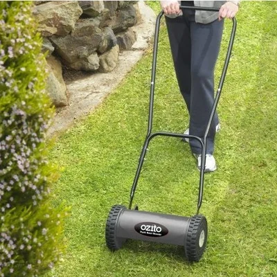 A woman pushing a black manual push mower across a green lawn