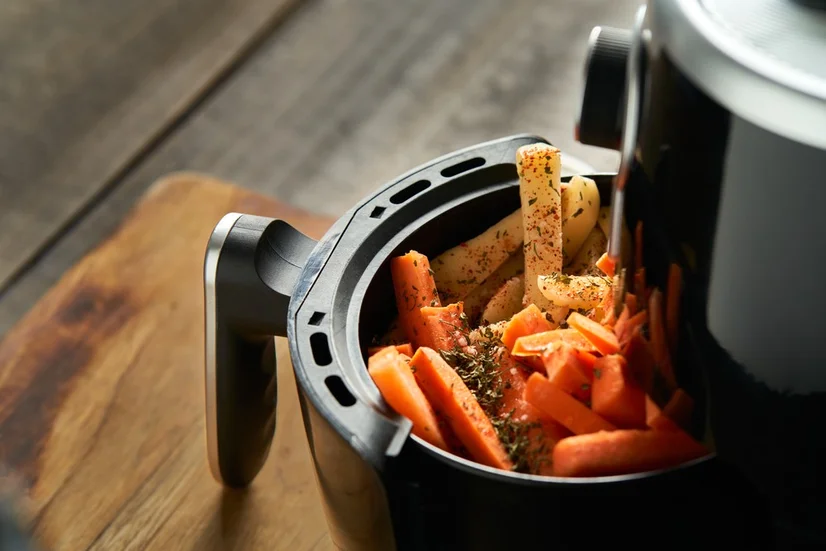 An air fryer with potato and sweet potato chips covered in seasoning in the basket.