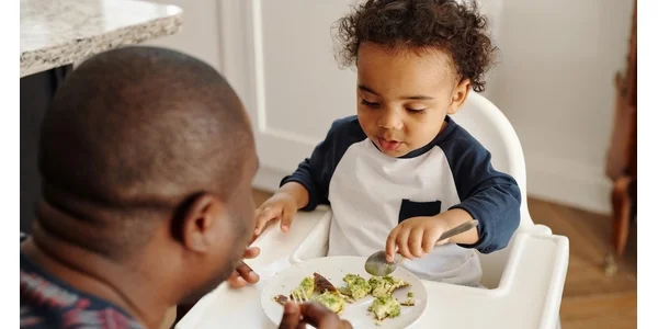 A child sitting in his high chair and eating pasta off a plate.
