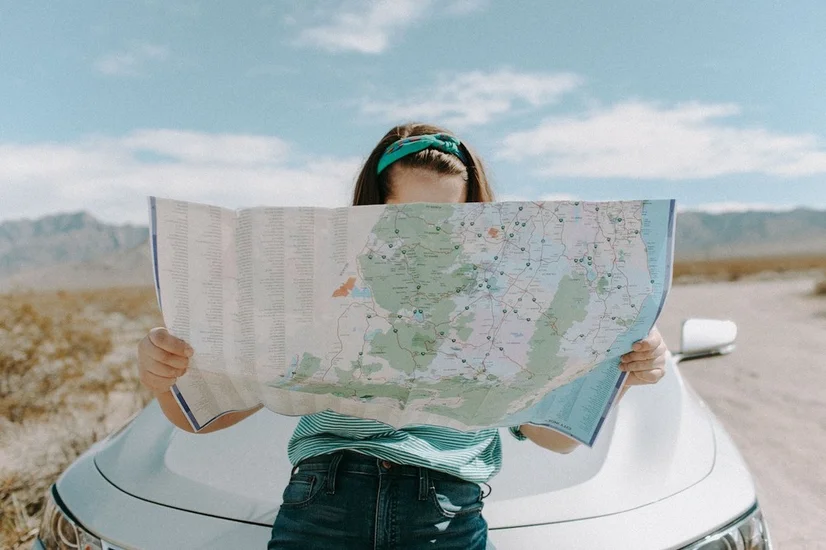 A woman consulting a map while leaning on the hood of her car in a National Park.