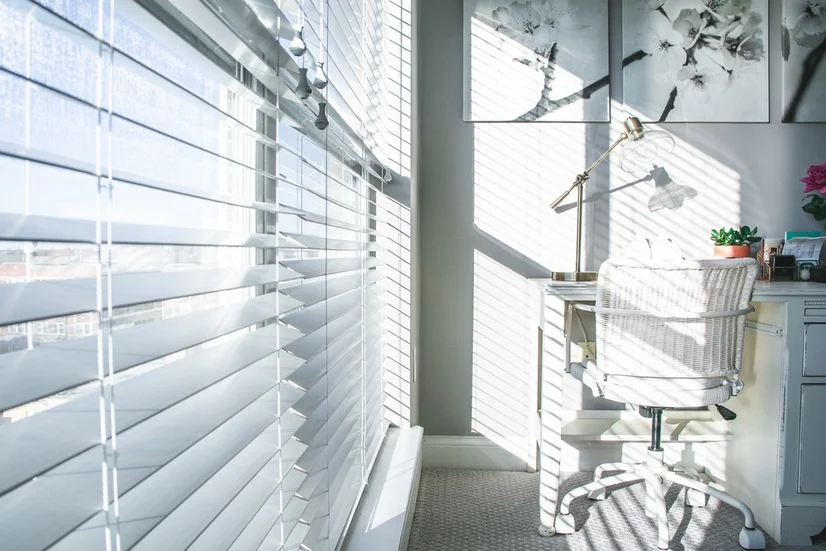 White Venetian blinds letting in light into a home office.