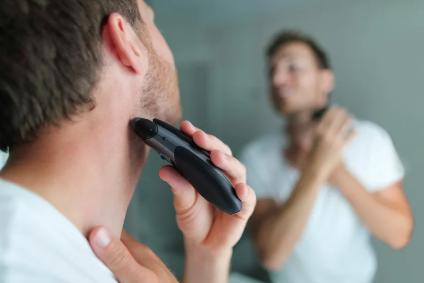 A man using an electric shaver on his neck in front of a mirror