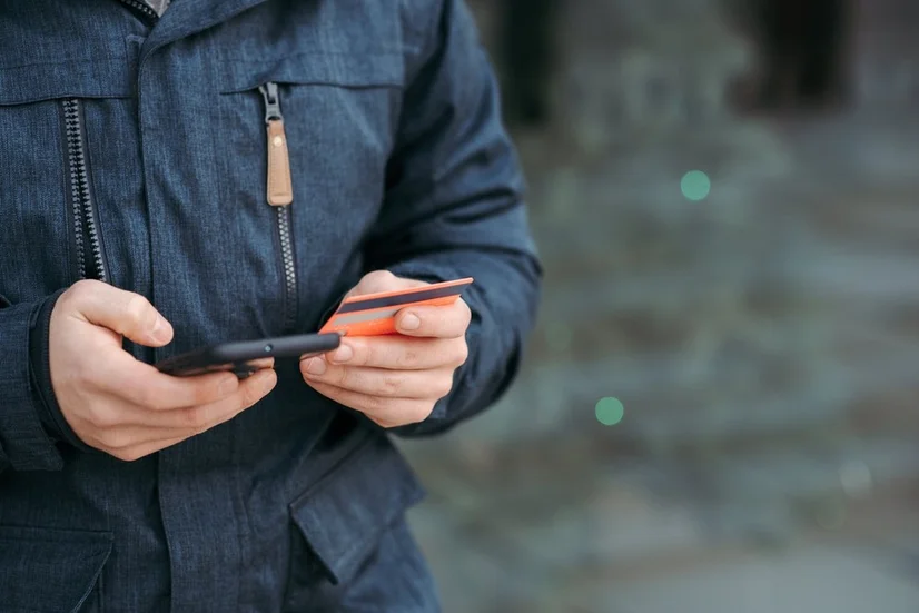 A man wearing a blue jacket entering his debit card details into his smartphone.