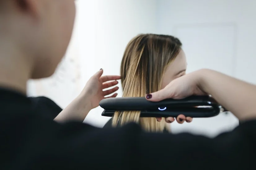 A hair stylist using a hair straightener to straighten the hair of a woman