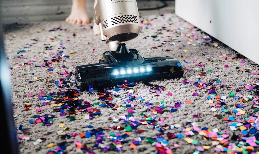 A vacuum cleaner with an LED light vacuuming up confetti from a carpet.