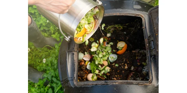 A woman turning on a black portable speaker sitting on her desk. There's a laptop and a glass of water in the background.