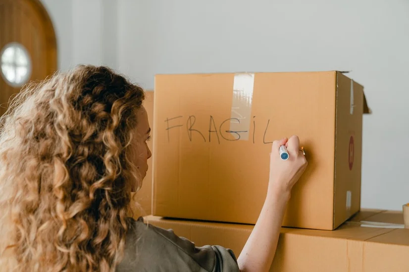 Woman writing 'Fragile' on a cardboard box