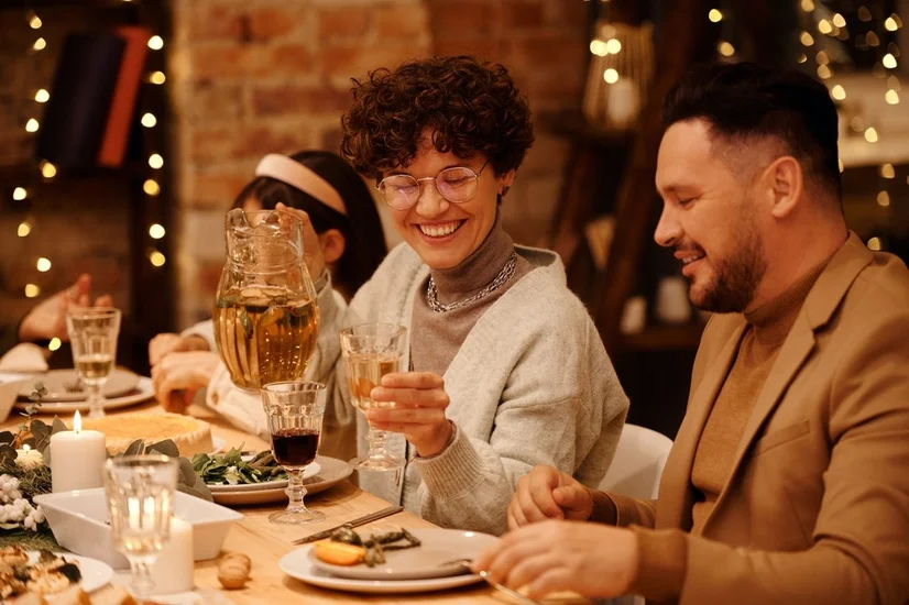 A woman pouring a drink for a man at a table set with a Christmas dinner.