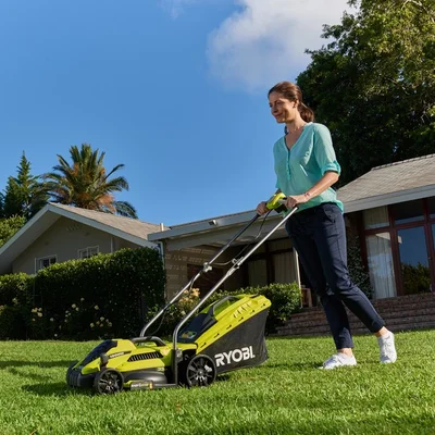 A woman pushing a green and black electric lawn mower acrodd her backyard