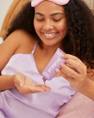 A woman squirting some of the Peppy Co. All-in-One Sleeping Mask into her hand.