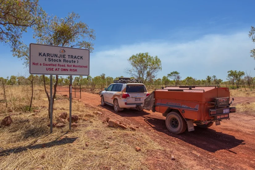 A 4WD towing an orange camper trailer along a dirt track.