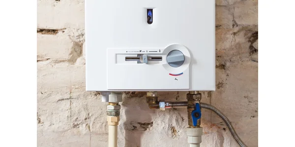 A gas hot water system mounted on a white brick wall.