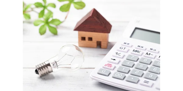 A model house, a lightbulb, and a calculator on a desk.