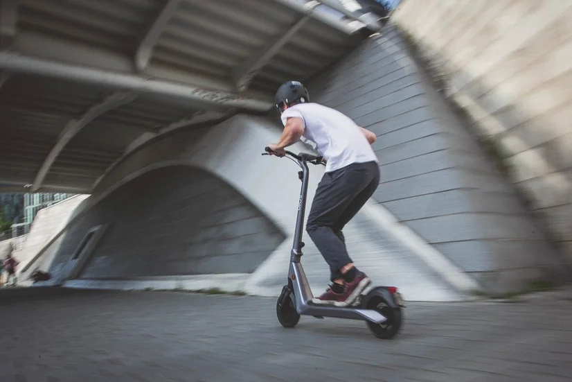 Man with helmet riding an electric scooter on pavement underneath a bridge