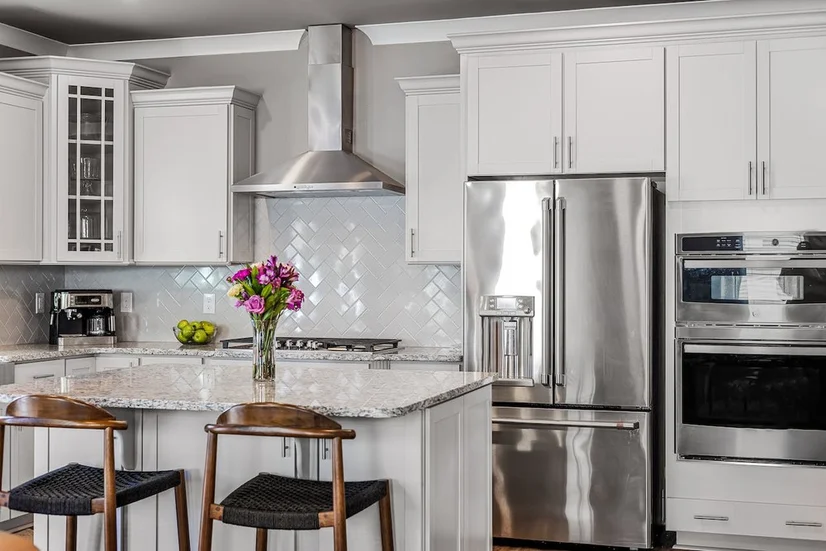A stainless steel French door fridge in a modern kitchen with white cabinetry.