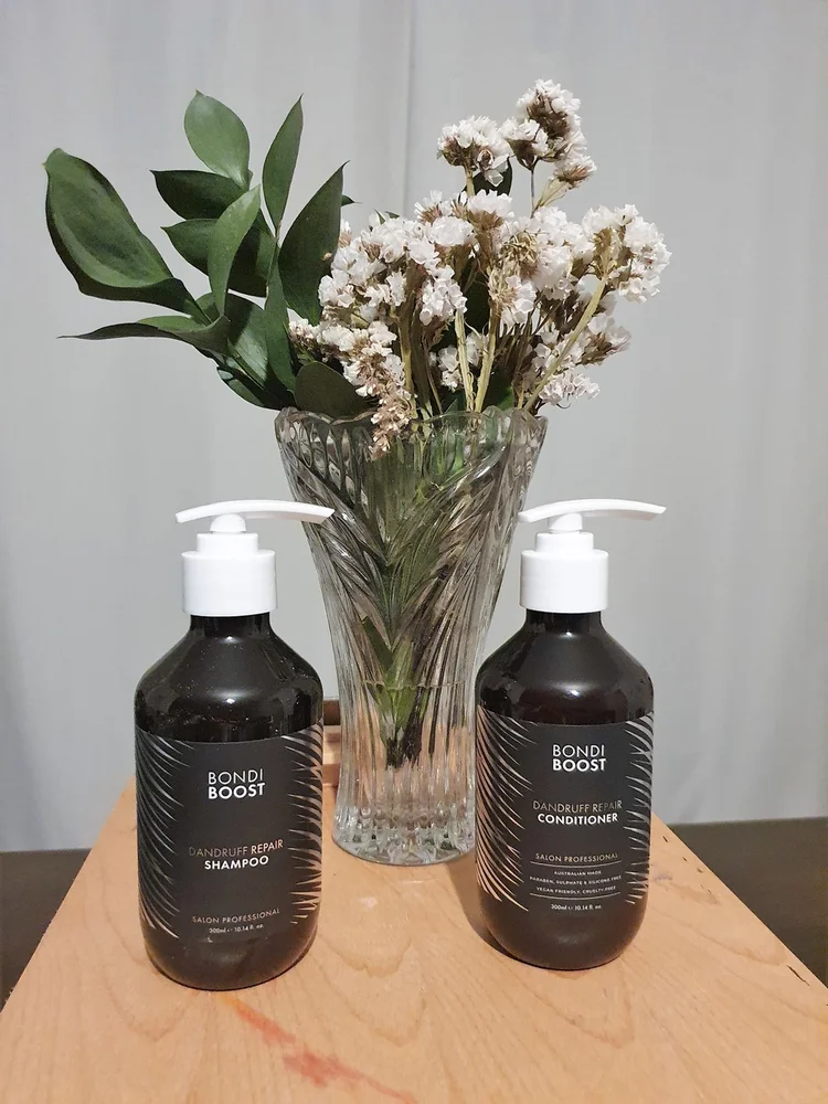 bondi boost dandruff reapir shampoo and conditioner on timber stand with white flowers in vase background