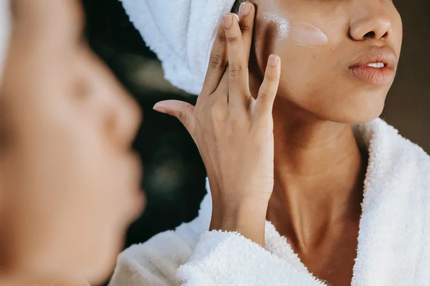 woman in robe applying cream to her face