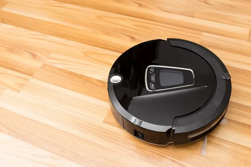 A black robot vacuum cleaning a hardwood floor