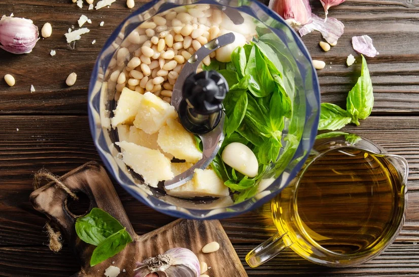 A food processor bowl filled with ingredients to make basil pesto.