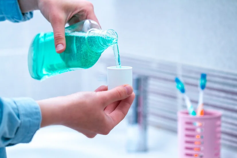 Man pouring bright green minty mouthwash into a cup after brushing and flossing