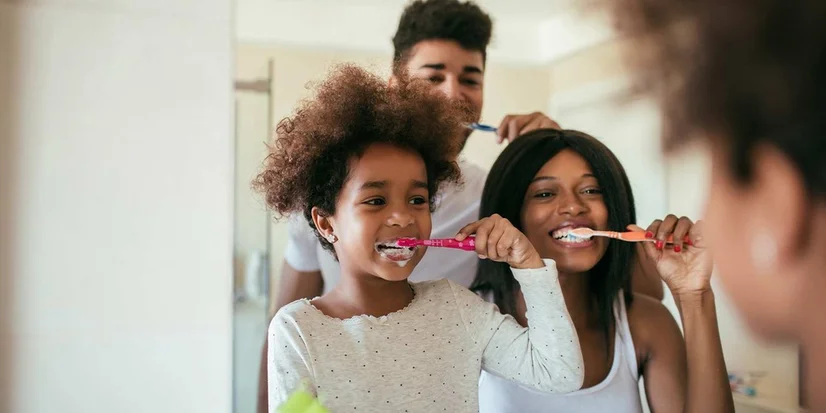 Family of three happily brushing teeth in front of mirror