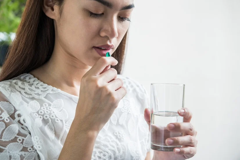 Woman taking a vitamin pill with glass of water