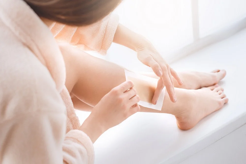 Woman at home applying a wax strip to her leg