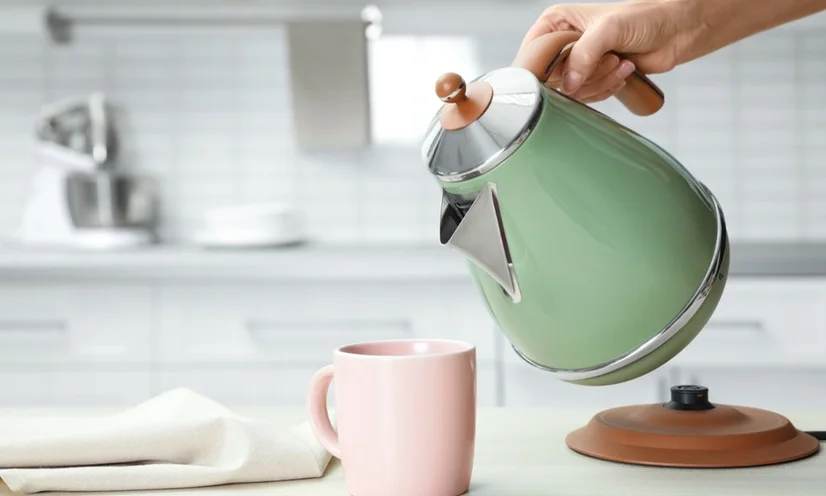 Someone using a retro-looking green electric kettle to pour water into a pastel pink mug.