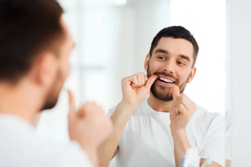 Man standing in front of mirror flossing teeth